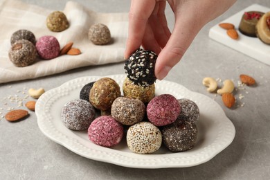 Photo of Woman taking delicious vegan candy ball from plate at table, closeup