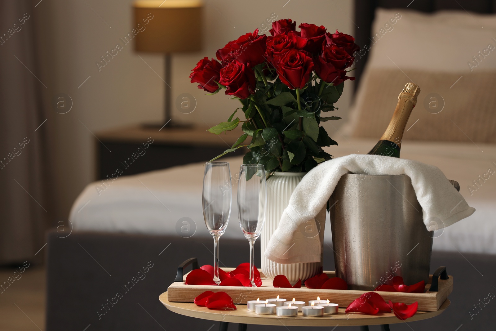 Photo of Honeymoon. Sparkling wine, glasses and bouquet of roses on wooden table in room. Space for text