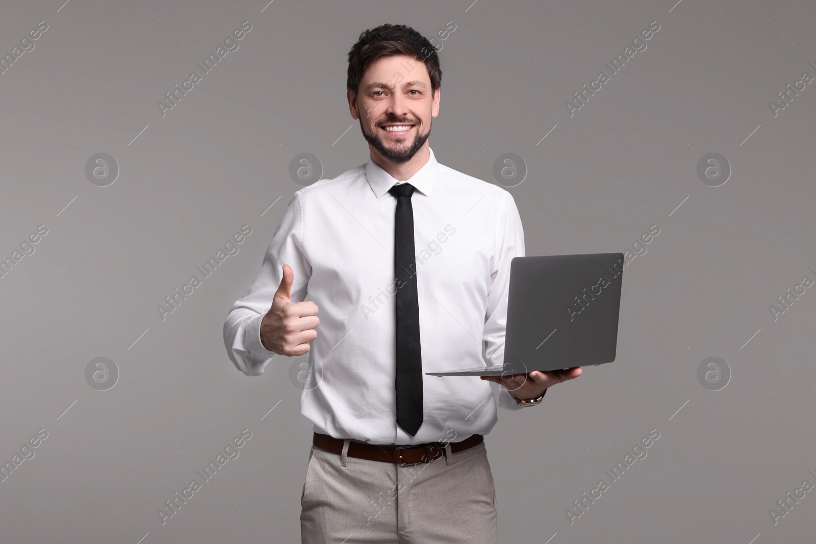 Photo of Happy man with laptop showing thumb up gesture on grey background