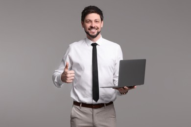 Photo of Happy man with laptop showing thumb up gesture on grey background