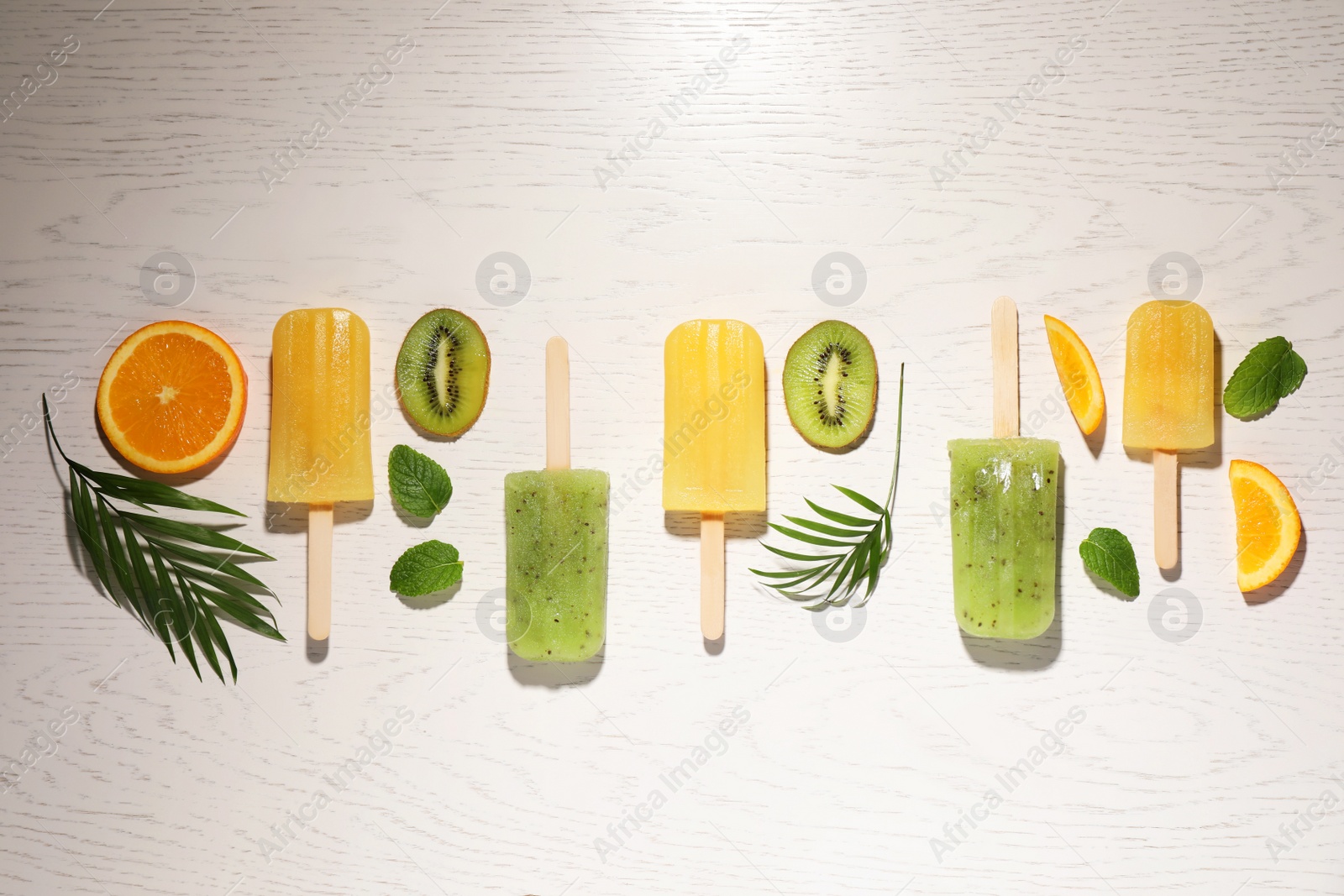 Photo of Tasty orange and kiwi ice pops on white wooden table, flat lay. Fruit popsicle