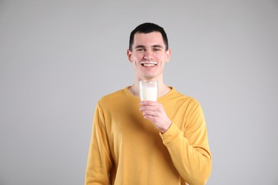 Photo of Happy man with milk mustache holding glass of tasty dairy drink on gray background