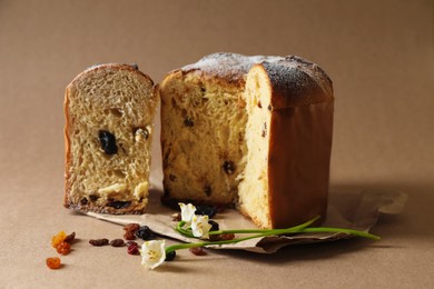 Photo of Delicious cut Panettone cake, raisins and beautiful flowers on light brown background. Traditional Italian pastry