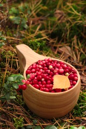 Photo of Many tasty ripe lingonberries and autumn leaf in wooden cup outdoors
