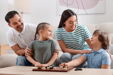 Parents playing checkers with children at table in room