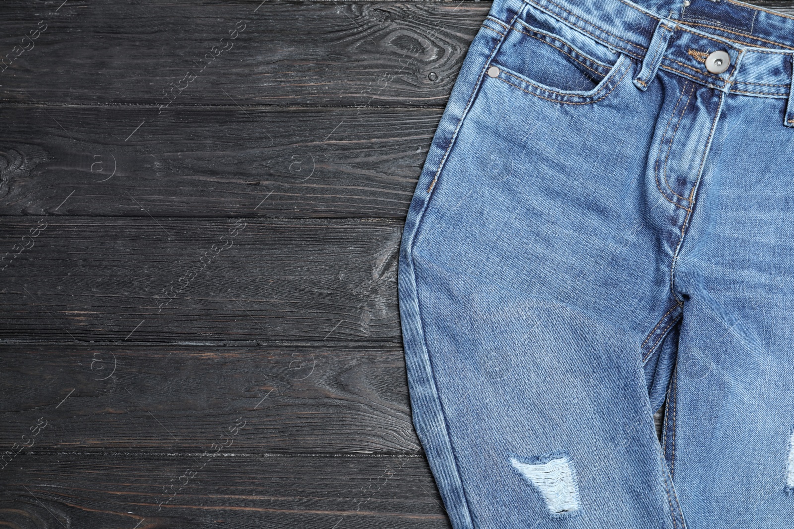 Photo of Stylish jeans on black wooden background, top view. Space for text