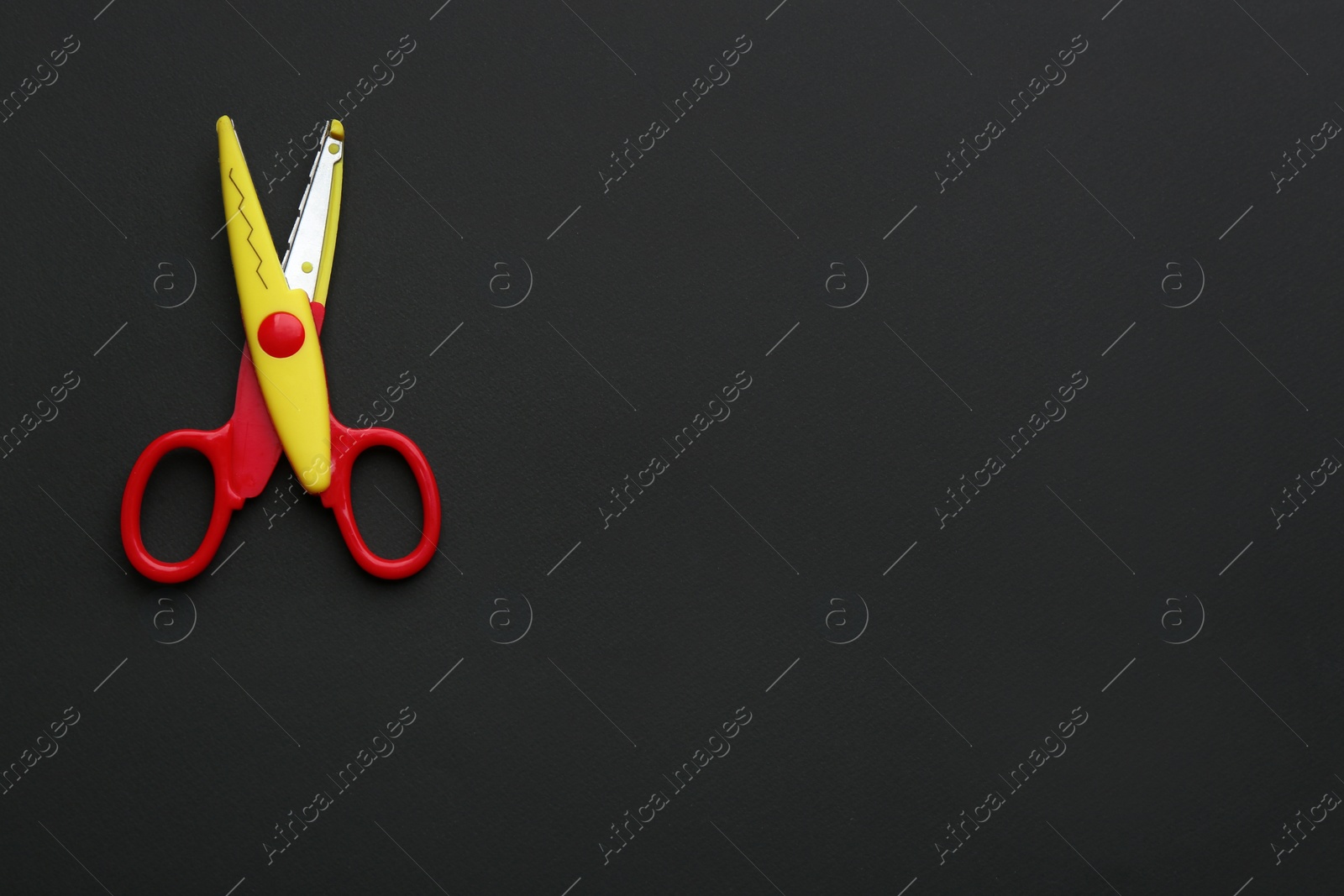 Photo of Decorative edge scissors on dark background, top view. Space for text