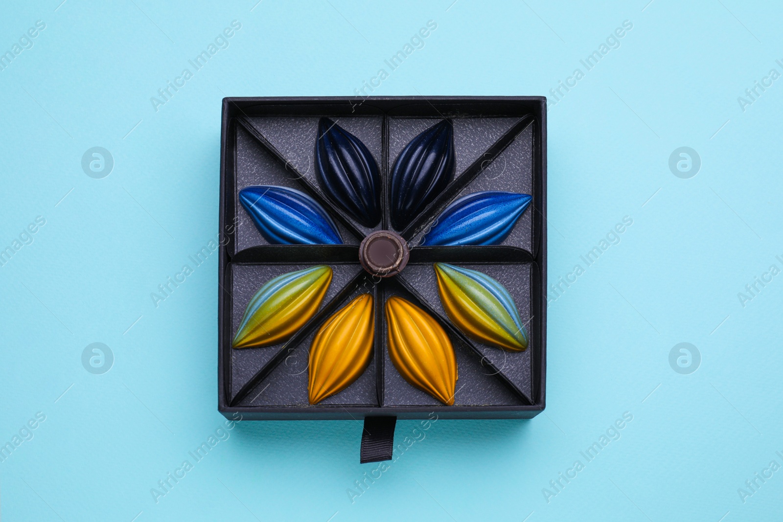 Photo of Box of tasty chocolate candies on light blue background, top view
