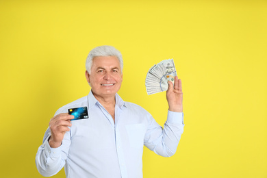 Photo of Happy senior man with cash money and credit card on yellow background