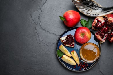 Photo of Honey, pomegranate, apples and shofar on black table, flat lay with space for text. Rosh Hashana holiday