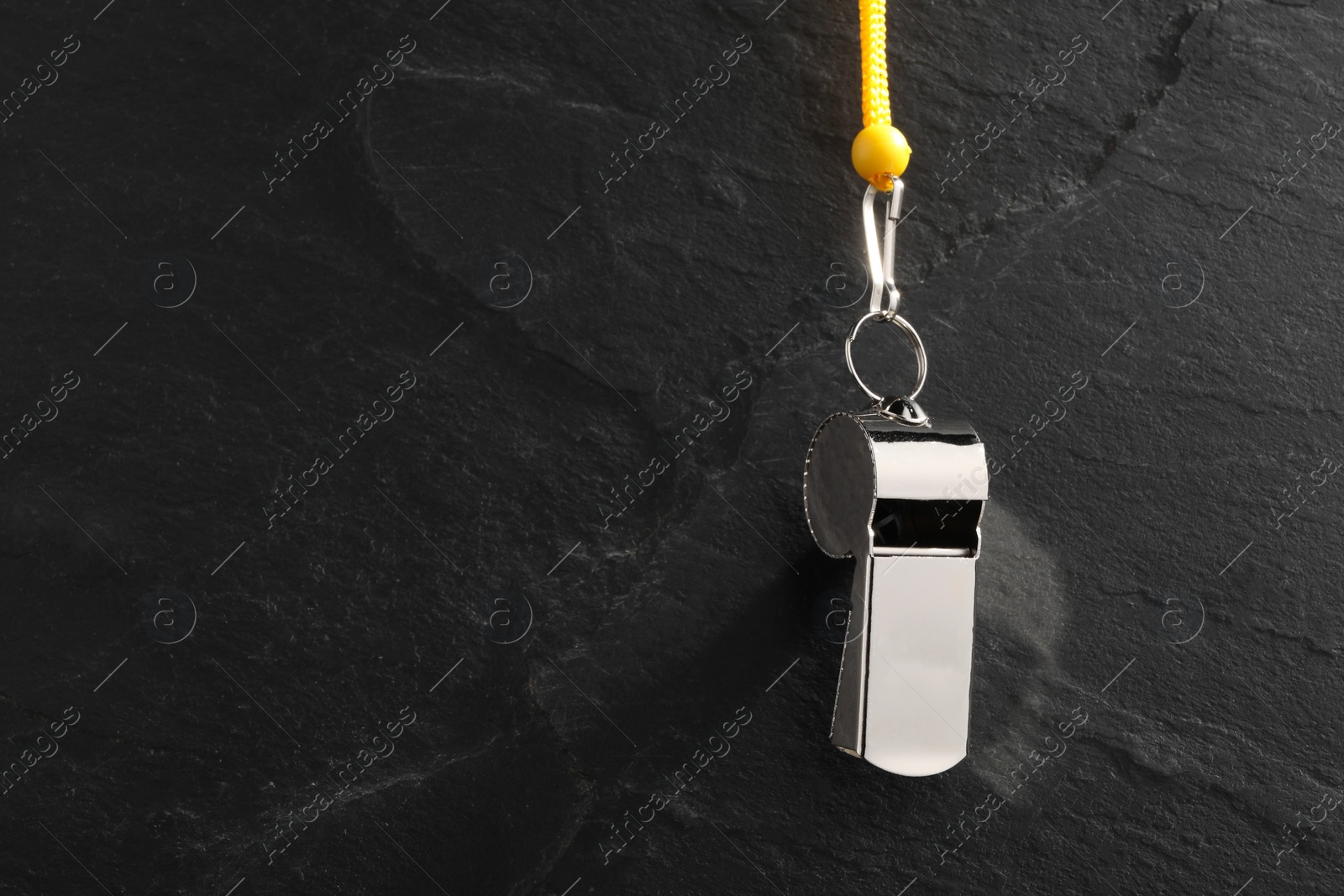 Photo of Referee equipment. Metal whistle on black textured background, closeup and space for text