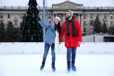 Happy couple skating along ice rink outdoors