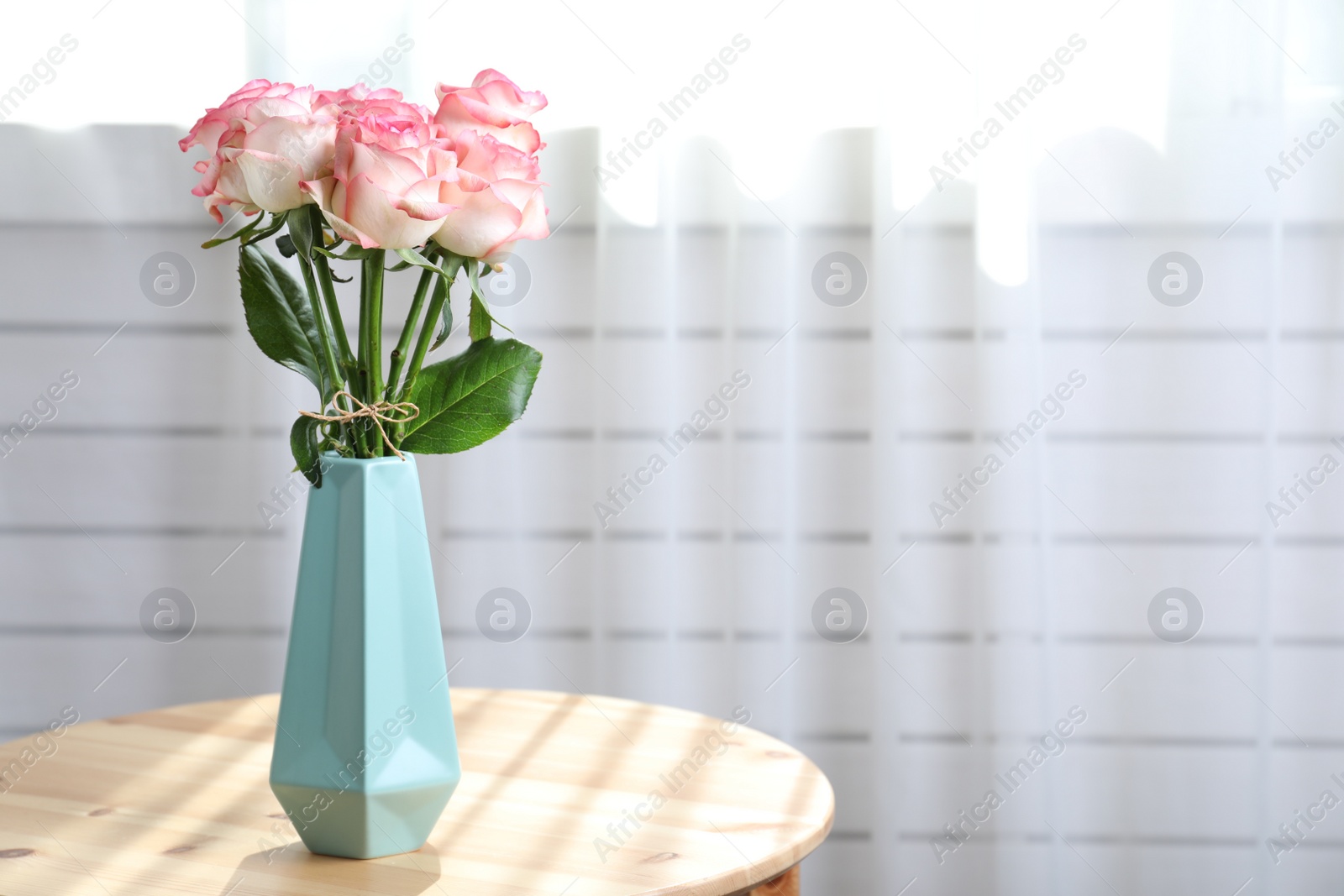 Photo of Vase with beautiful pink roses on wooden table in room. Space for text