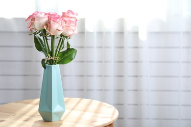 Photo of Vase with beautiful pink roses on wooden table in room. Space for text