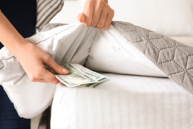 Photo of Woman hiding dollar banknotes under blanket in bedroom, closeup. Money savings