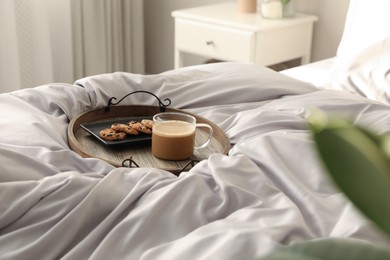 Photo of Delicious cookies and cup of coffee on bed with stylish silky linens indoors