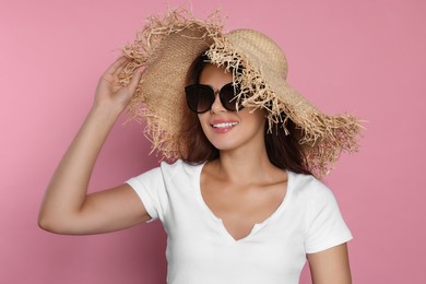 Happy beautiful woman with stylish straw hat and sunglasses on pink background