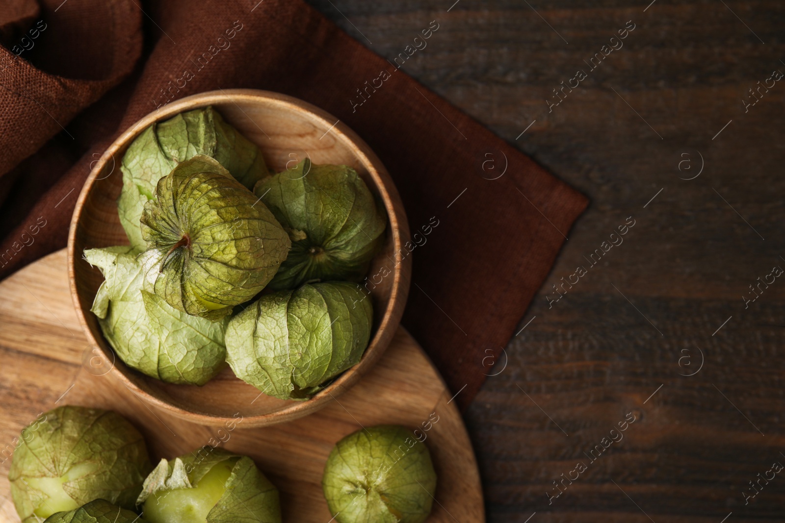 Photo of Fresh green tomatillos with husk in bowl on wooden table, top view. Space for text