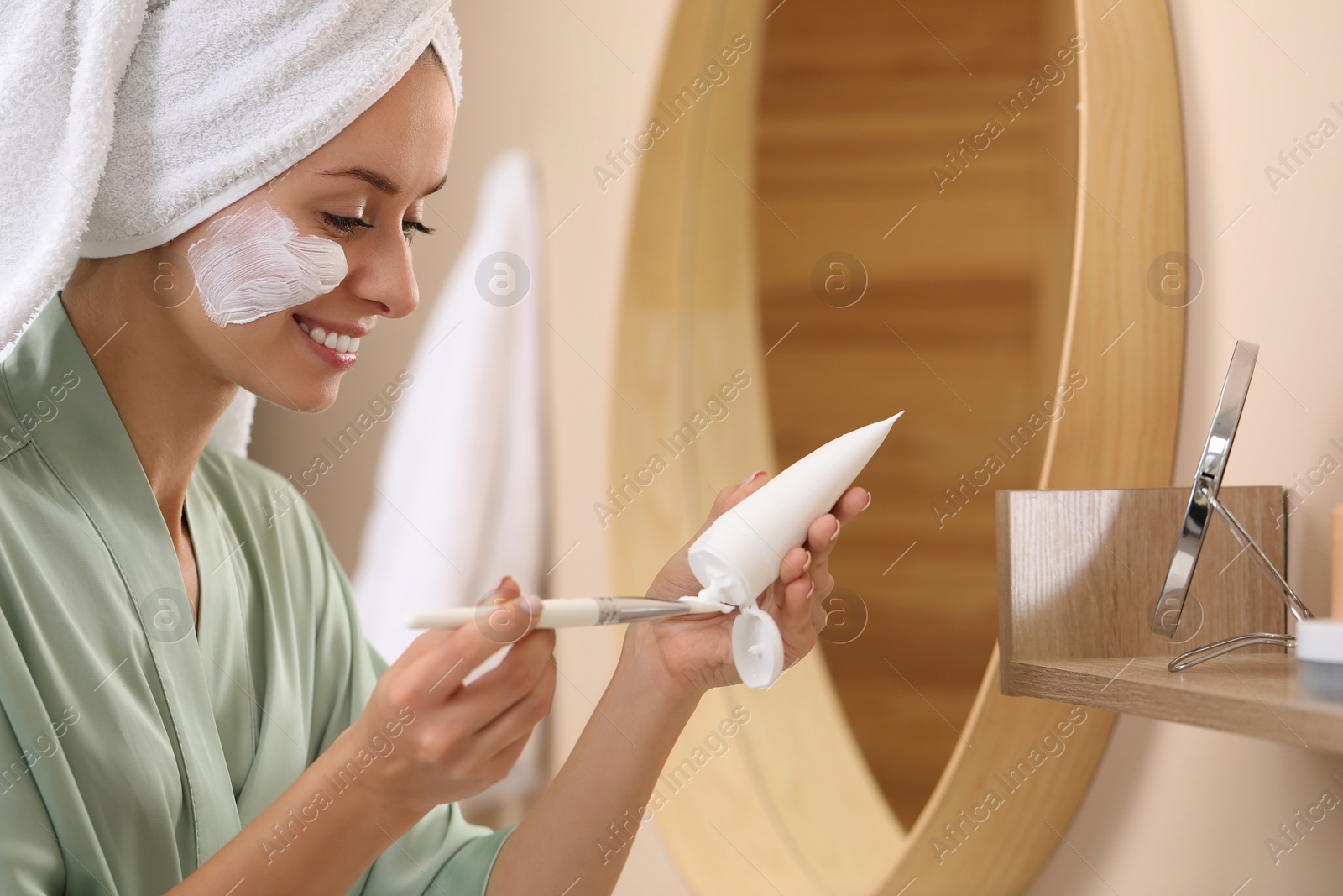 Photo of Woman applying face mask onto brush in bathroom. Spa treatments