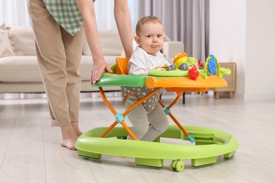 Cute boy making first steps with baby walker. Mother and her little son spending time together at home