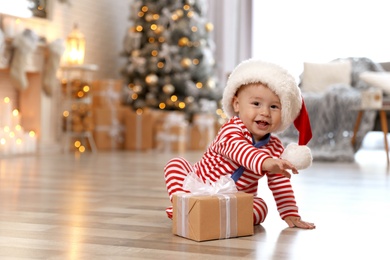 Photo of Little baby with Santa hat and Christmas gift on floor at home