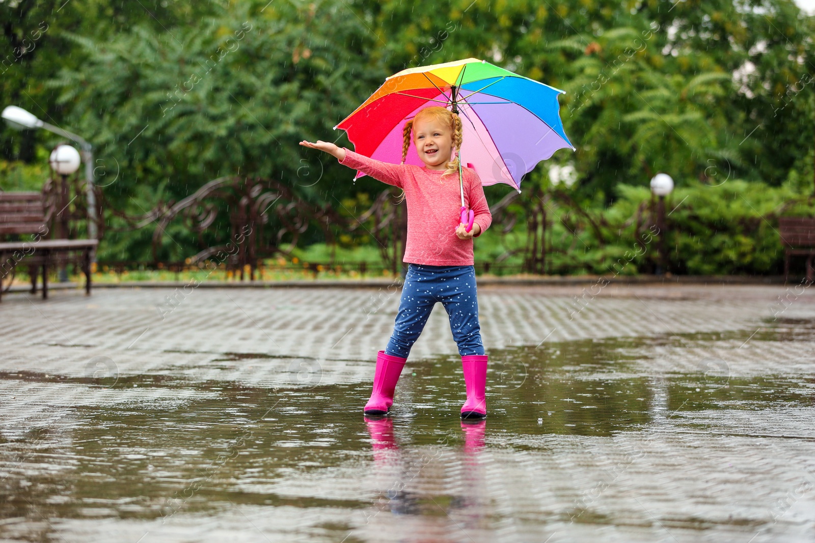 Photo of Cute little girl with bright umbrella under rain on street