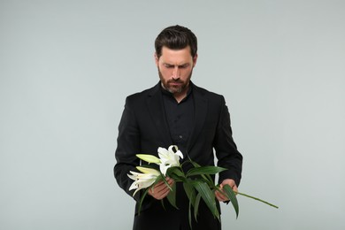 Sad man with white lilies on light grey background. Funeral ceremony