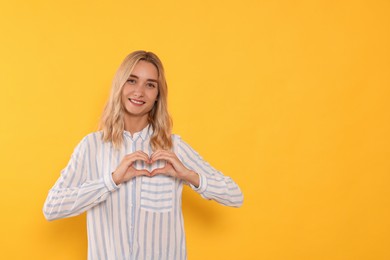 Photo of Happy volunteer making heart with her hands on orange background. Space for text