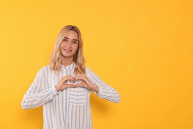 Happy volunteer making heart with her hands on orange background. Space for text