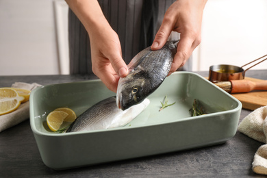 Photo of Woman putting dorada fish into baking dish, closeup