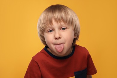 Photo of Cute boy showing his tongue on orange background