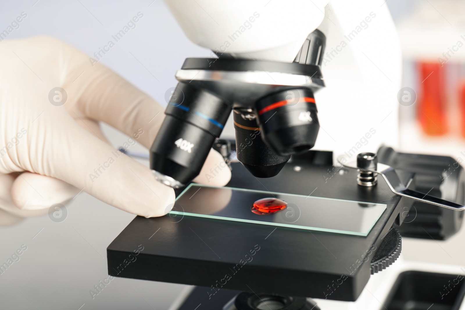 Photo of Scientist examining sample of red liquid on slide under microscope in laboratory, closeup