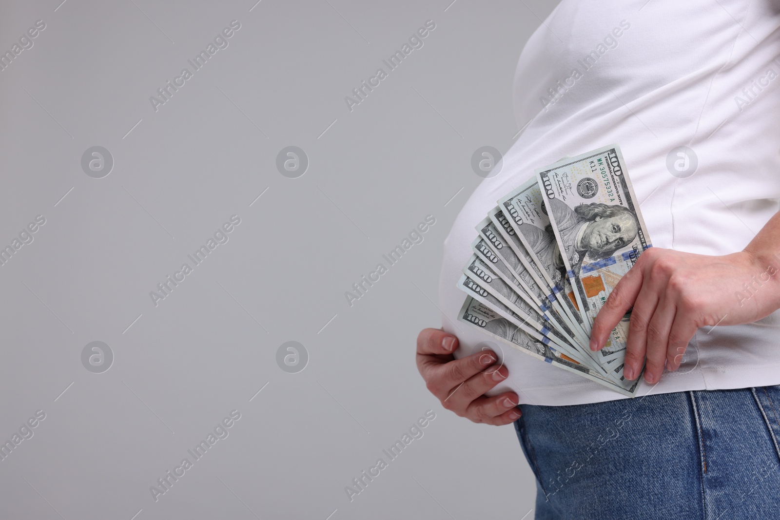 Photo of Surrogate mother. Pregnant woman with dollar banknotes on light grey background, closeup. Space for text