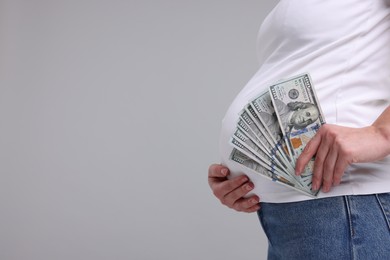 Photo of Surrogate mother. Pregnant woman with dollar banknotes on light grey background, closeup. Space for text