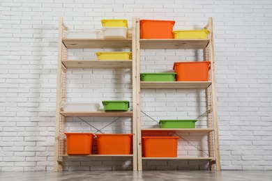 Wooden shelving units with colorful containers near white brick wall. Stylish room interior