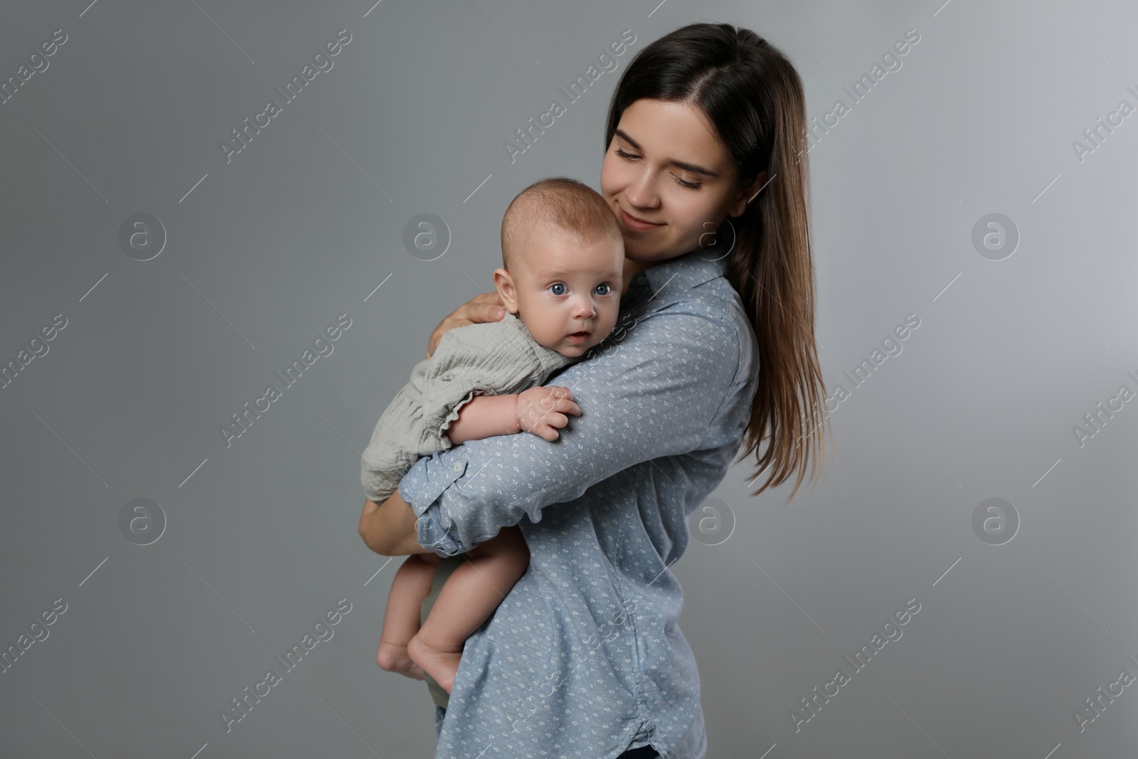 Photo of Beautiful mother with her cute baby on grey background