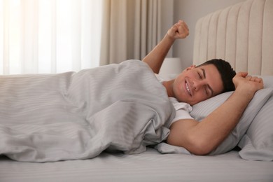 Photo of Man stretching in bed with grey linens at home