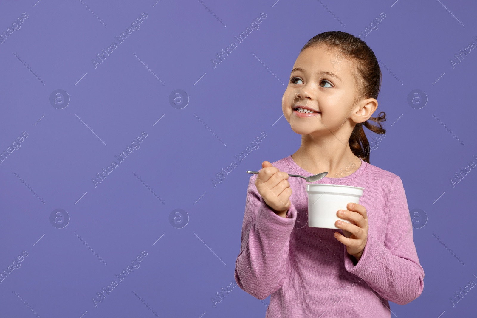Photo of Girl with tasty yogurt on violet background, space for text