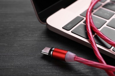Photo of Red USB cable with type C connector and laptop on black wooden table, closeup