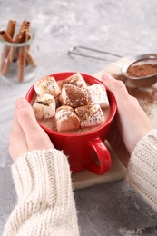 Woman drinking aromatic hot chocolate with marshmallows and cocoa powder at gray table, closeup