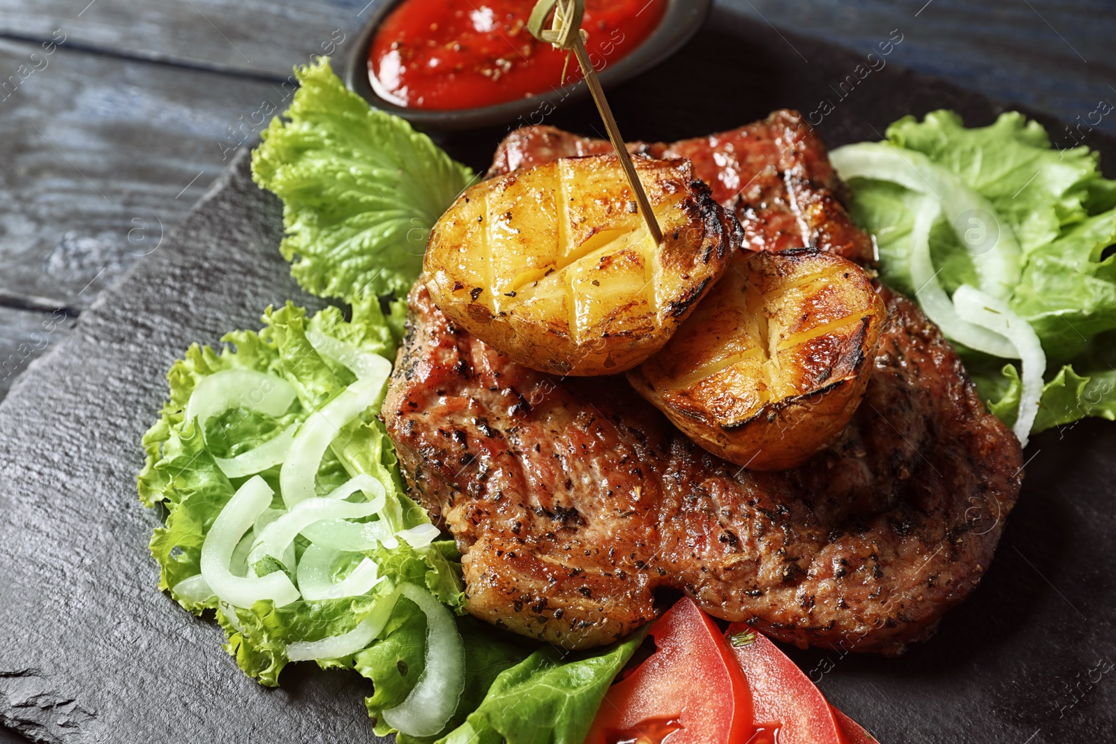 Photo of Tasty grilled meat and potatoes served on slate plate, closeup