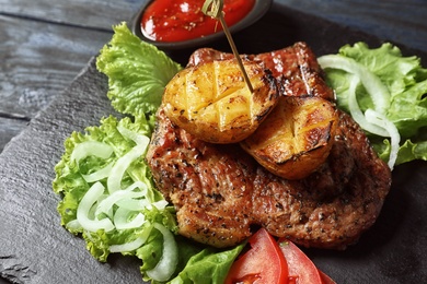 Photo of Tasty grilled meat and potatoes served on slate plate, closeup