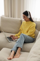 Woman with laptop and headphones sitting on sofa at home