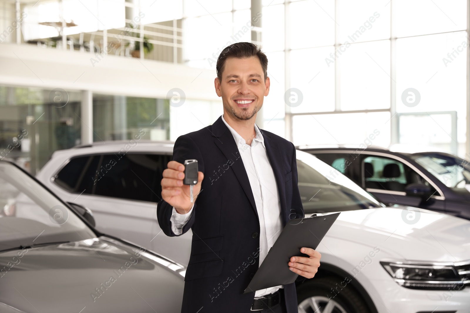 Photo of Salesman with clipboard and car key standing in salon