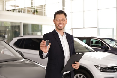 Salesman with clipboard and car key standing in salon