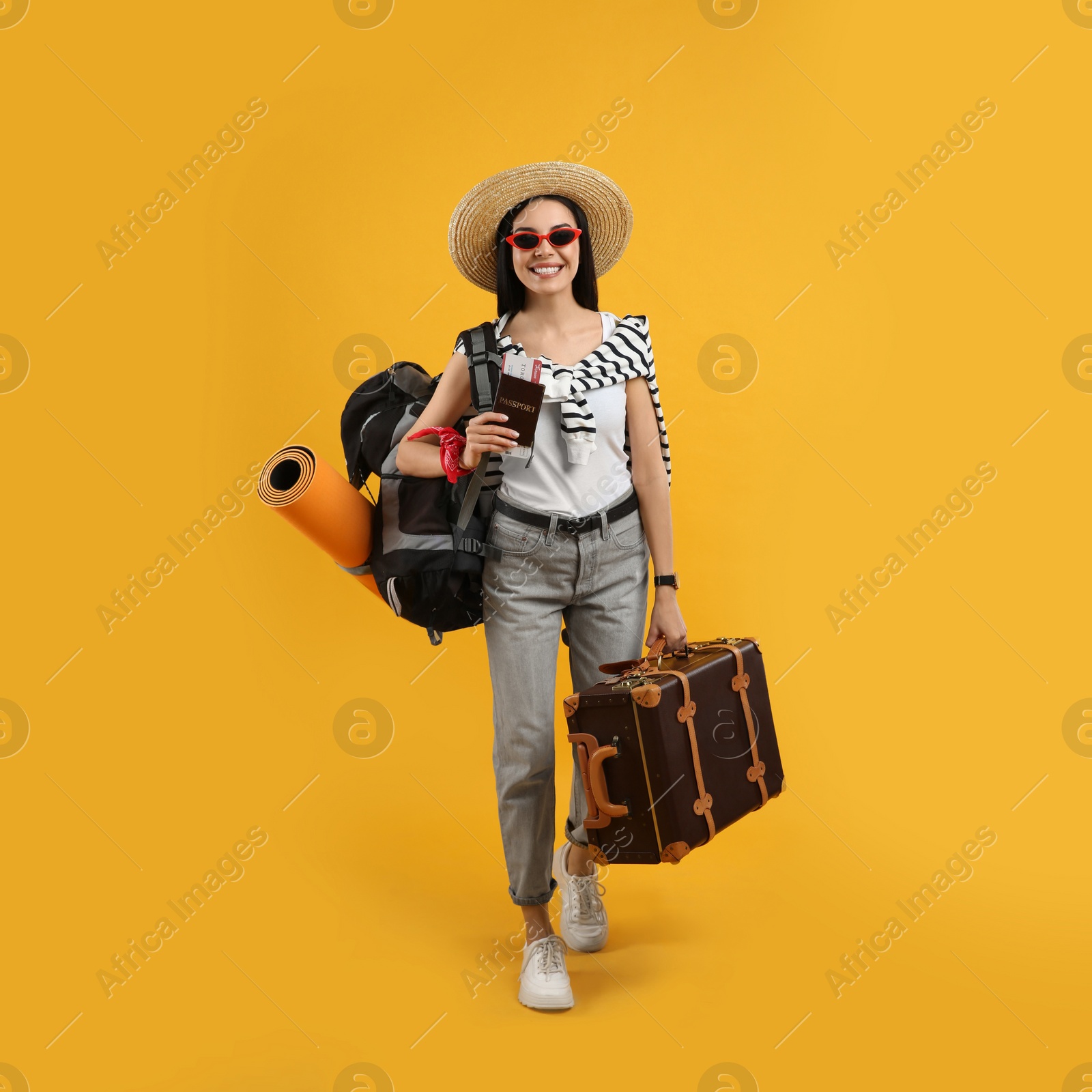 Photo of Happy female tourist with passport, suitcase and backpack on yellow background