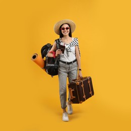 Happy female tourist with passport, suitcase and backpack on yellow background
