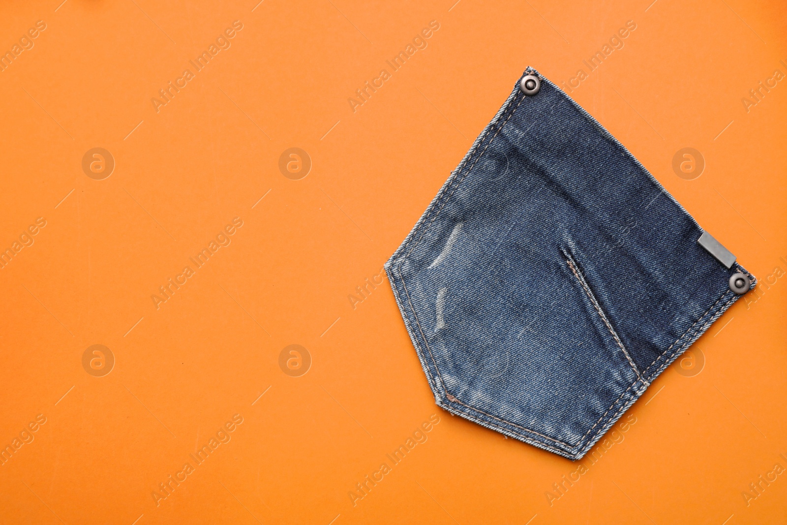 Photo of Stylish jeans pocket on orange background, top view. Space for text