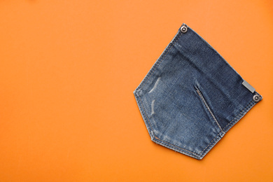 Photo of Stylish jeans pocket on orange background, top view. Space for text