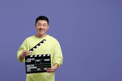 Photo of Happy asian actor with clapperboard on purple background, space for text. Film industry
